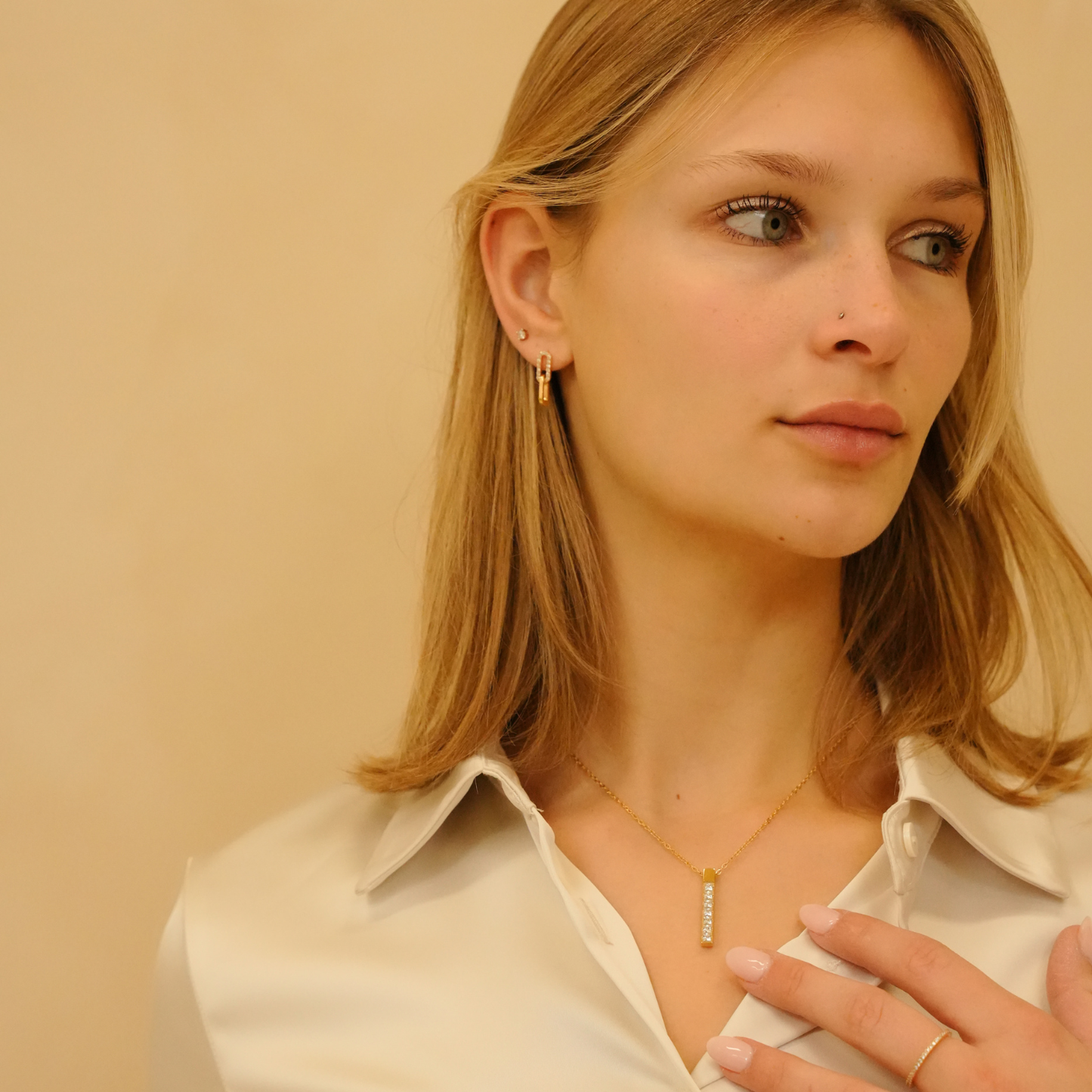 Gold stud earrings with zirconia, styled with a gold necklace and a cream-colored shirt.