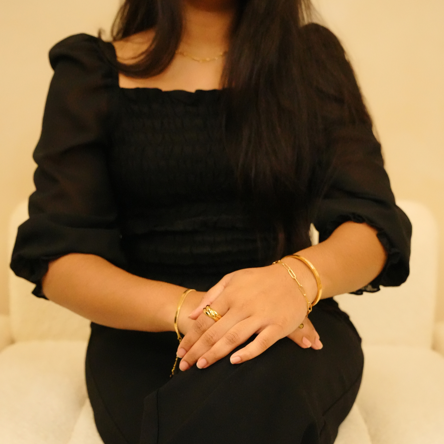 Gold bracelet with stone detail, worn with a ring and long-sleeved black top.