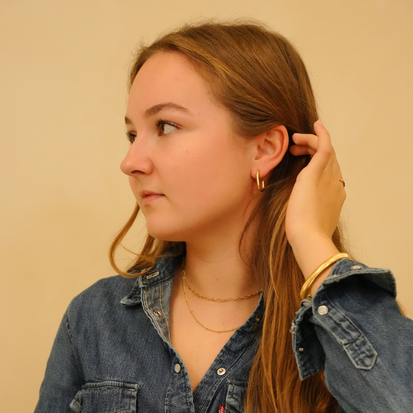 Gold bracelet, from an unknown brand, on a woman in a denim shirt.
