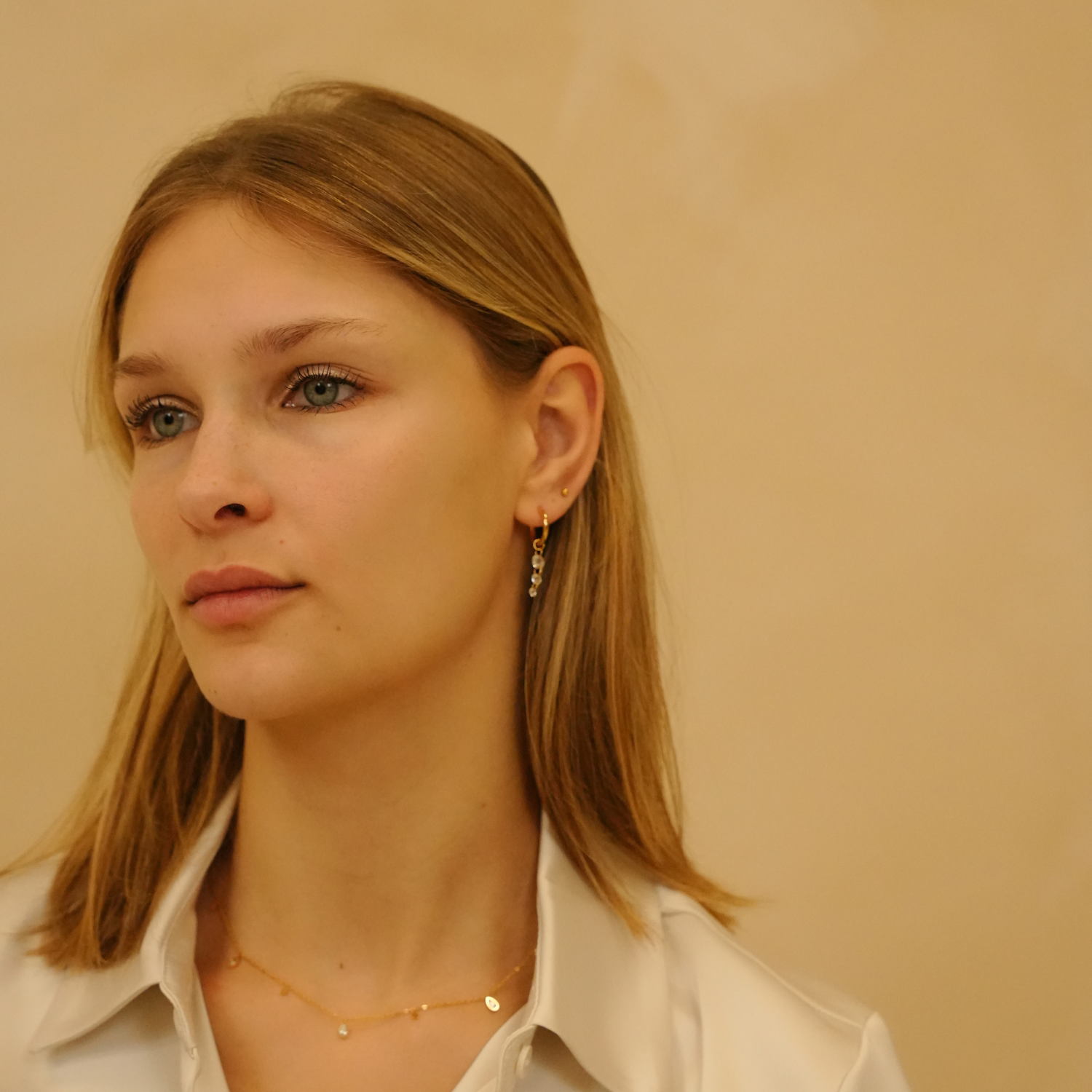 Gold starlight hoop earrings with gem embellishments and wire closures, worn with a gold necklace and cream-colored blouse.
