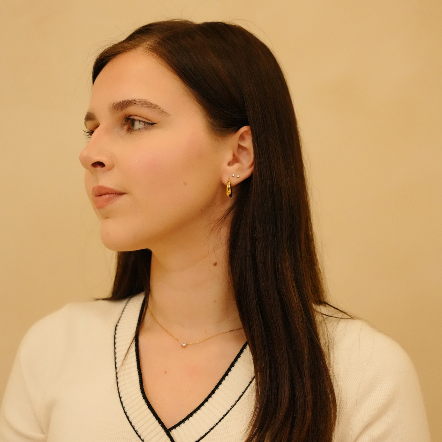 Elegant zirconia necklace with a delicate gold chain, featuring a small stone, accented by gold hoop earrings and a white sweater.