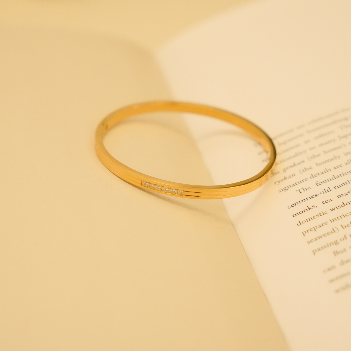 Gold bracelet with stones by OMAI, resting on an open book.