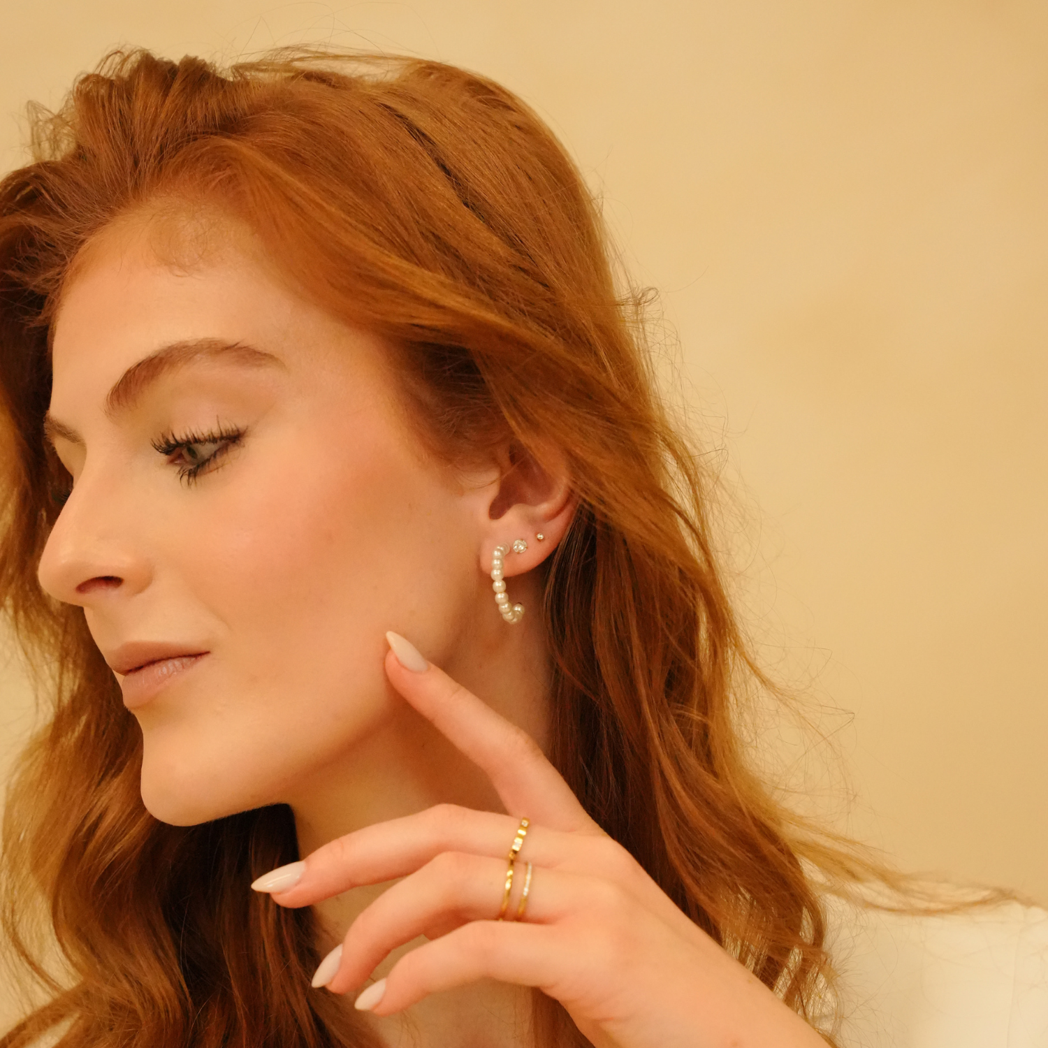 Pearl hoop earrings by an unknown brand, shown on a model with red hair, with gold rings on the fingers.