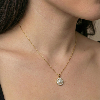 Gold pearl necklace by Amour, featuring a round pendant with crystal halo, worn on a woman.