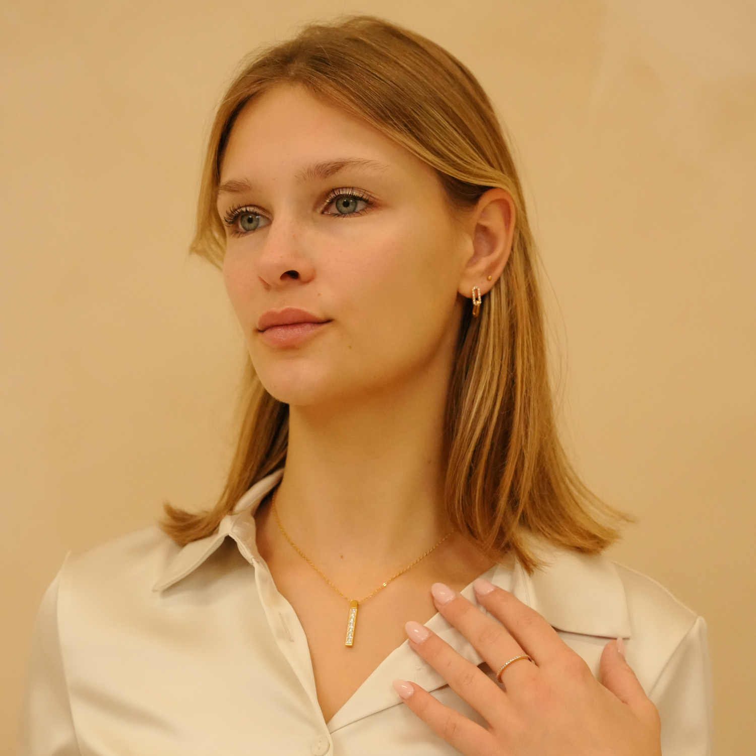 Zirconia ring with gold band by Timeless Spark featuring dainty detailing, worn with a gold necklace and white blouse.

