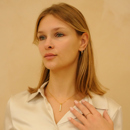 Zirconia ring with gold band by Timeless Spark featuring dainty detailing, worn with a gold necklace and white blouse.
