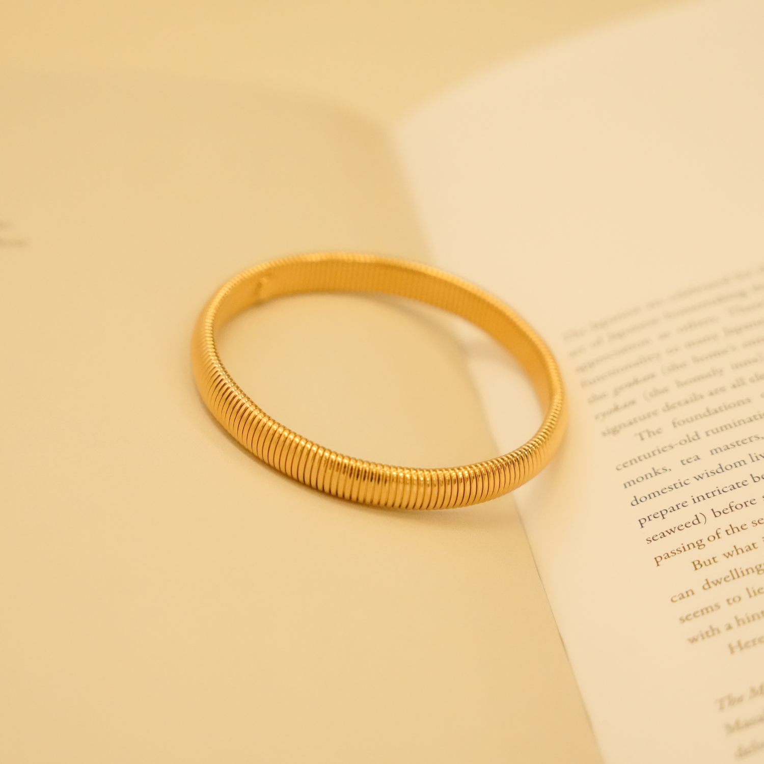 Gold flexible bracelet from an unidentifiable brand with a ribbed design and smooth texture.