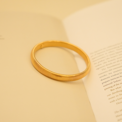 Gold flexible bracelet from an unidentifiable brand with a ribbed design and smooth texture.