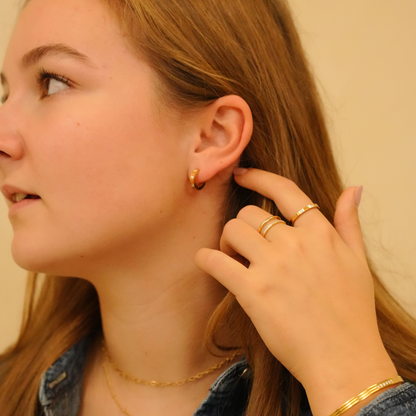 Gold hoop earrings with stones worn in ear, paired with gold rings and bracelet on hand.
