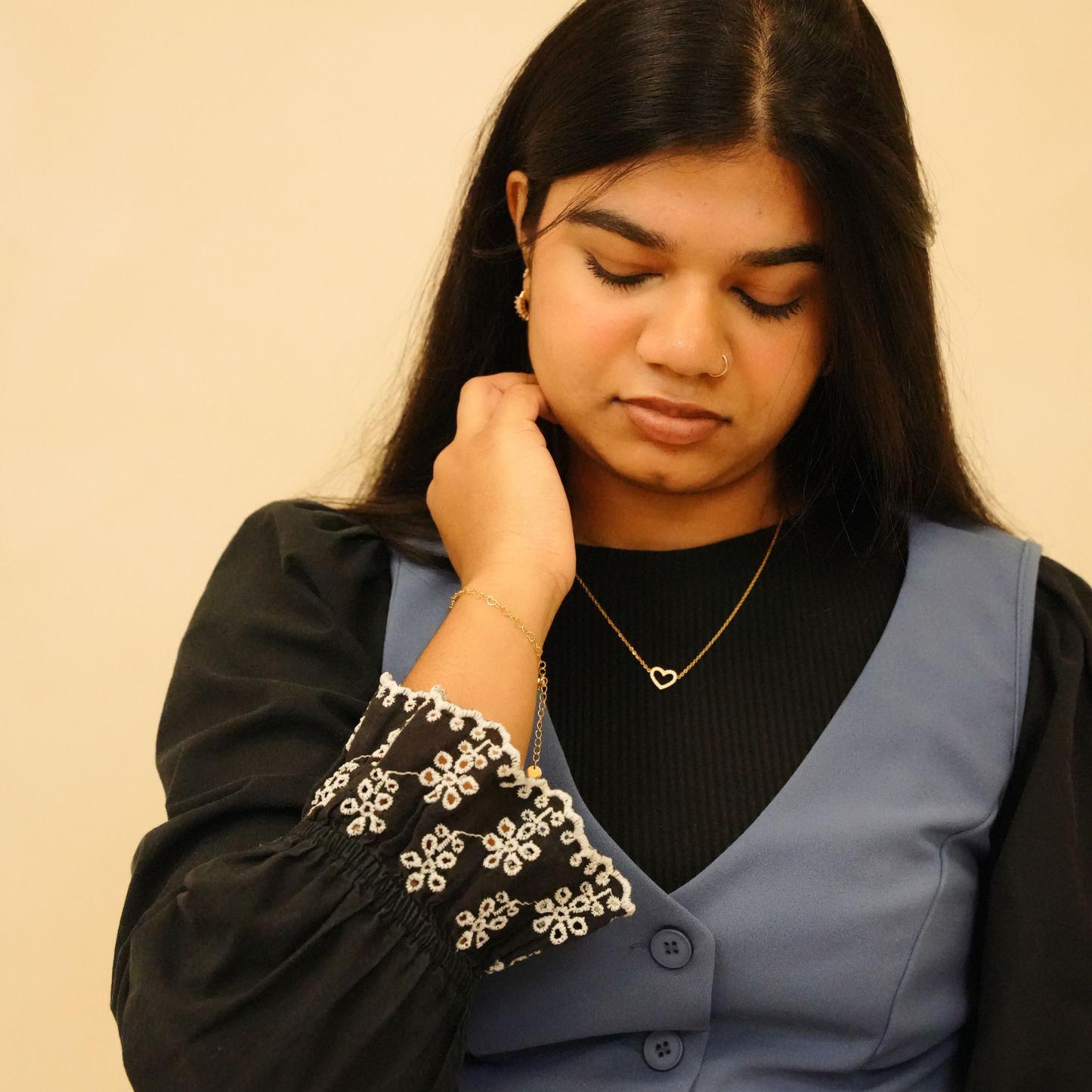 Gold heart necklace with thin chain featuring a hollow heart pendant, alongside other visible jewelry.