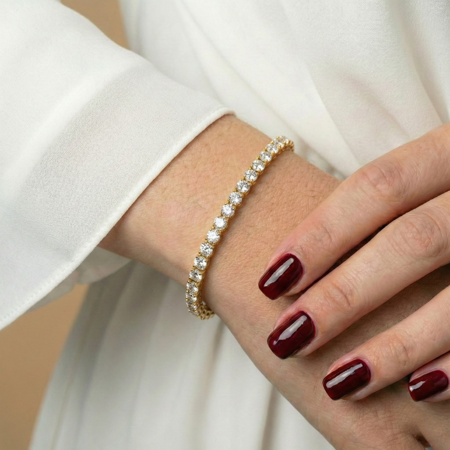 Gold bracelet with white stones by Chérie, on a wrist with dark red manicure.