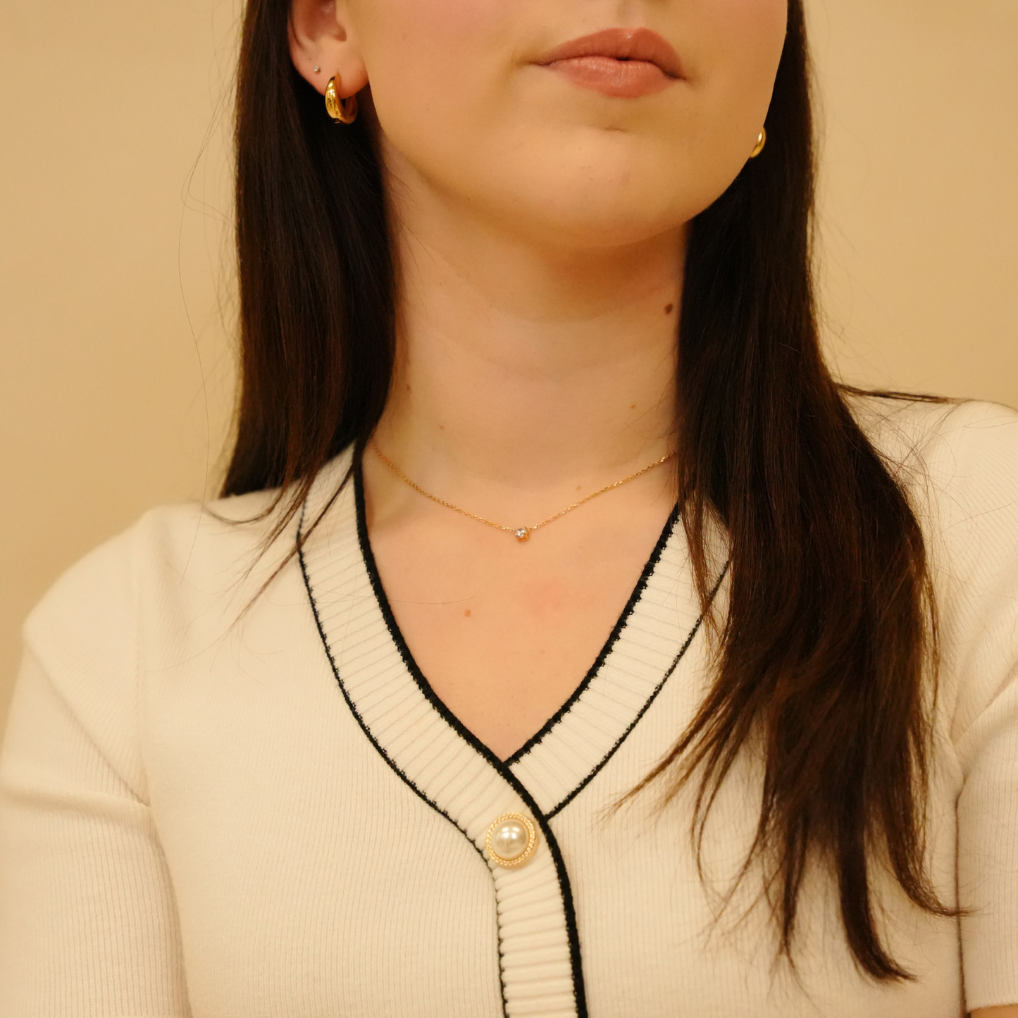 Elegant zirconia necklace with golden chain, featuring a small pendant, and worn with hoop earrings.
