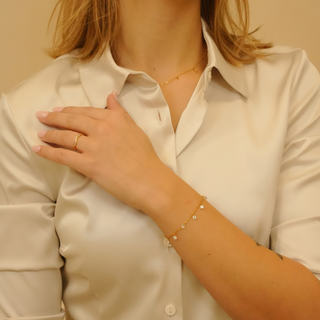 Gold charm bracelet with dangling stones by unknown brand, worn with a ring and satin button-down shirt.