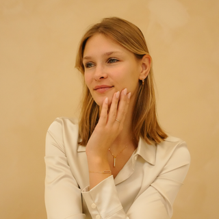 Gold zirconia earrings from Dainty Glow, worn with a gold necklace and bracelet, against a neutral background.
