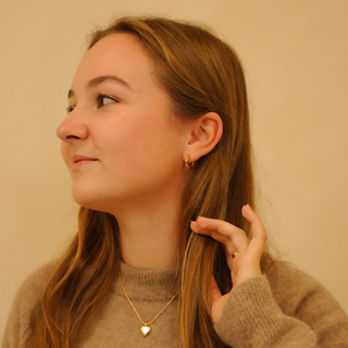 Elegant gold hoop earrings with no brand attribution, styled with a gold heart pendant necklace and a brown sweater.
