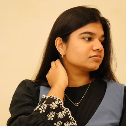 Gold heart necklace with chain, featuring a simple heart pendant, worn with black and blue top.
