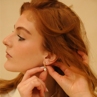 Ivy zirconia stud earrings from an angled side view, with a woman's hand fastening one.
