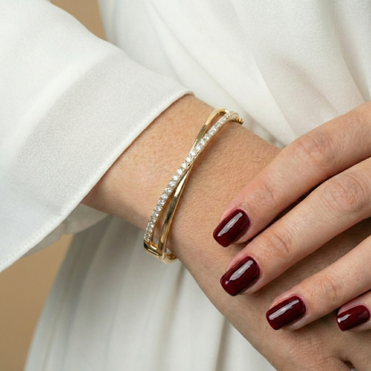 Gold bracelet with diamonds by Bisou, styled on a model with maroon nail polish and a white shirt.
