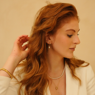 Goldtone flexible bracelet with ribbed detailing, worn with a pearl necklace and white jacket.