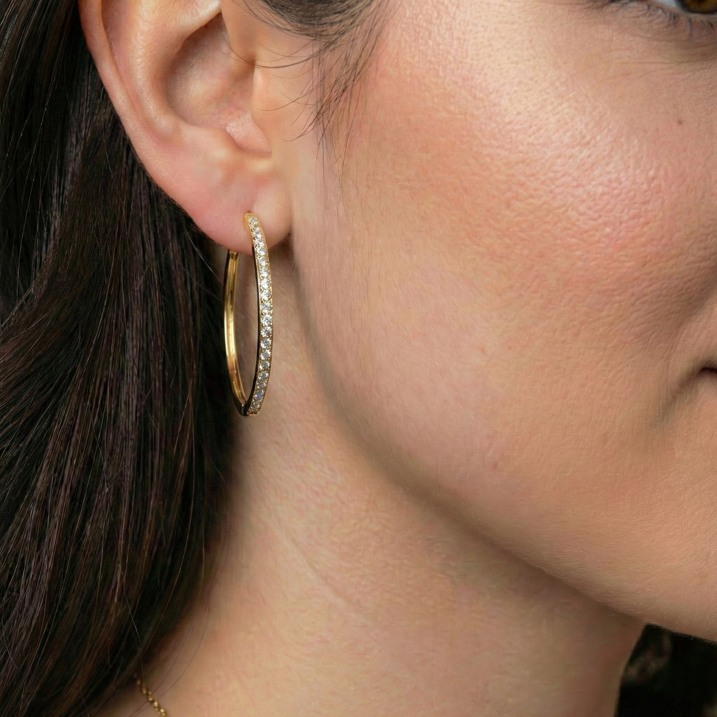 Close-up of a person wearing a gold hoop earring with small diamonds.