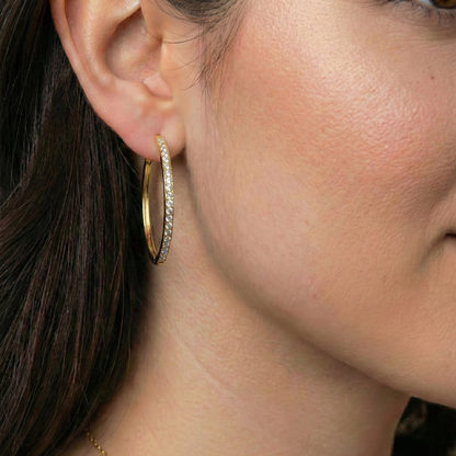 Close-up of a person wearing a gold hoop earring with small diamonds.